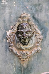 Antique door knocker in the shape of a human head on a wooden door in Venice, Italy