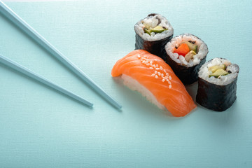 Sushi set with salmon nigiri and roll with cucumber and vegetables with chopsticks on a blue background, for the sushi bar menu