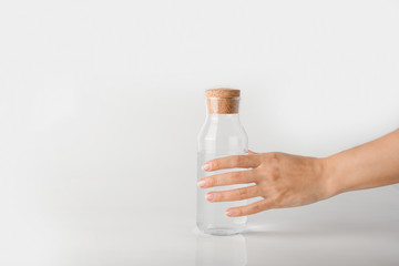 A hand takes a glass bottle filled with clear water on a white background.