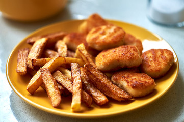 Tasty homemade potato french fries with chiken nuggets on yellow dish