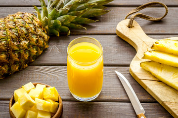 Pineapple juice in glass closeup near sliced fruit on wooden background