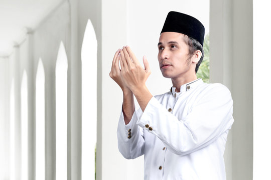Asian Muslim man standing while raised hands and praying