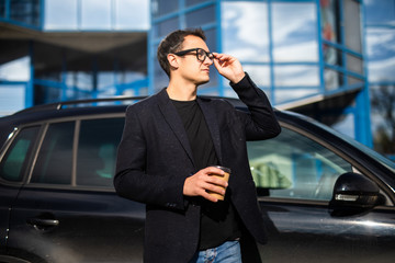 Intelligent male entrepreneur dressed in luxury suit walking near skyscrapers in financial district of megalopolis with coffee cup going to business meeting in downtown