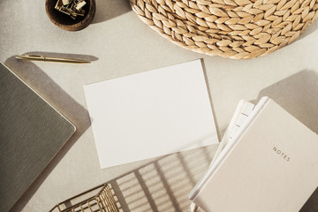 Flatlay blank paper sheet, notebooks, clips in wooden bowl, straw stand on beige concrete...