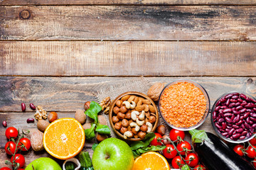 Concept of healthy vegan food, clean eating. On wooden background: vegetables, fruits, nuts, beans, lentils. Ripe seasonal product for clean meal. Copy space, flat lay, top view