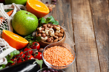 Concept of healthy vegan food, clean eating. On wooden background: vegetables, fruits, nuts, beans, lentils. Ripe seasonal product for clean meal. Copy space for text