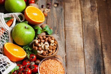 Concept of healthy vegan food, clean eating. Fresh raw ingredients on wooden background: vegetables, fruits, nuts, beans and lentils. No plastic, eco-friendly shopping for zero waste. Copy space