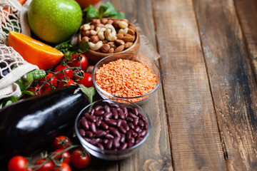 Concept of healthy vegan food, clean eating. Fresh raw ingredients on wooden background: vegetables, fruits, nuts, beans and lentils. No plastic, eco-friendly shopping for zero waste. Copy space