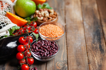 Concept of healthy vegan food, clean eating. Fresh raw ingredients on wooden background: vegerables, fruits, nuts, beans and lentils. No plastic, eco-friendly shopping for zero waste. Copy space