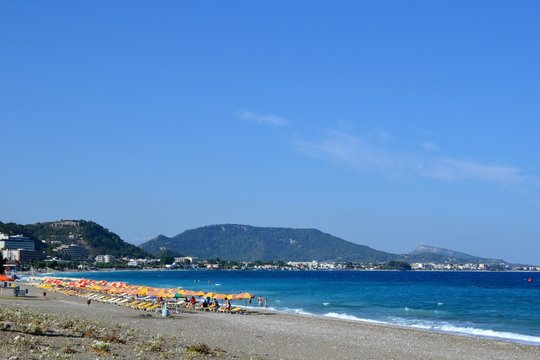 Ixia, Rhodes. People sunbathe and relax under colorful umbrellas on the pebble beach in Paralia/Ixia, on the north coast of the island, 4 km from the Rhodes town - island's capital