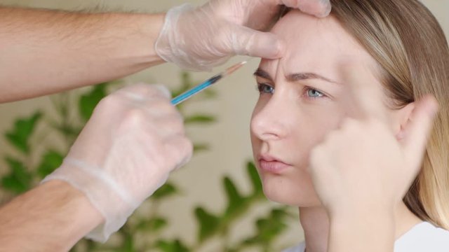 Close up of hands of expert beautician injecting botox in female forehead
