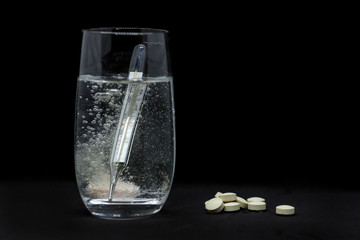 glass of water , thermometer and pills isolated on black background.