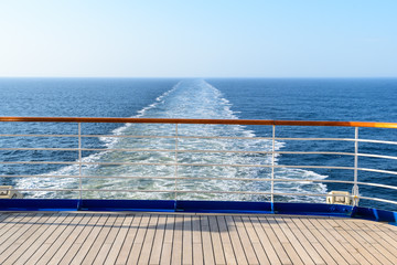 Aft deck of a wooden-coated cruise ship with railings. View of the wake waves behind the stern. Sea...