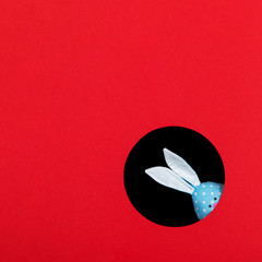 The concept, happy Easter, eared blue rabbit peeps out of the hole on red background. Copy space.