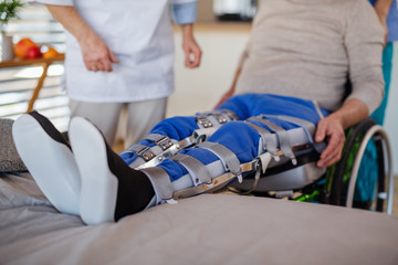 Unrecognizable healthcare worker and paralysed senior patient in hospital.