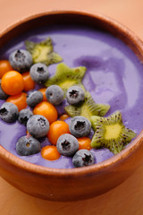 Smoothies of violet color from banana and currant, on top of a blackberry, physalis and kiwi berry. Smoothies in a wooden bowl.