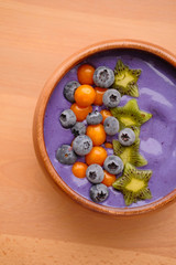 Smoothies of violet color from banana and currant, on top of a blackberry, physalis and kiwi berry. Smoothies in a wooden bowl.