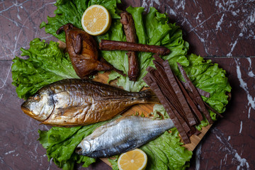 Beer snacks, dried and smoked fish, smoked neck, smoked quail, on a lettuce leaf, on a wooden plate.