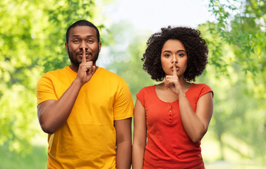 Obraz premium silence, secret and confidentiality concept - happy african american couple making hush gesture over green natural background