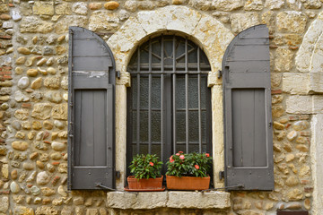 Fototapeta na wymiar Fenêtre à barreaux et volets bois sur vieux mur en pierres à Pérouges (01800), département de l'Ain en région Auvergne-Rhône-Alpes, France