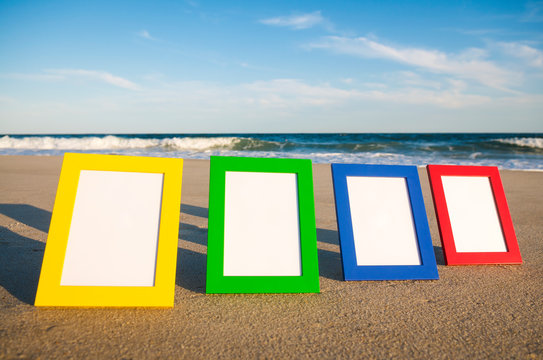 Row of simple colorful photo frames with blank image space lined up in the sun on an empty beach