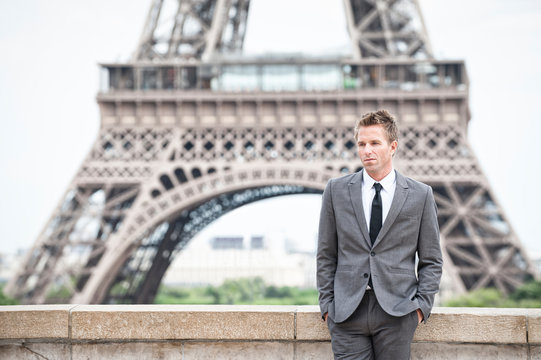 Serious European businessman standing alone in front of the Eiffel Tower in Paris, France