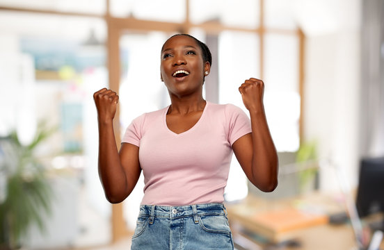 success, winning gesture and people concept - happy smiling young african american woman celebrating victory over office background
