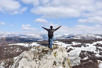 Tourist man is feeling free and standing with hands up on the top of the mountain. Climber enjoy in mountains in spring. Beautiful landscape