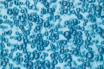 Fototapeta na wymiar Macro shot of air bubbles in transparent gel, blue background. Many spheres reflecting each other. Abstract pattern