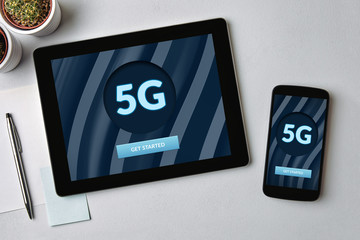5G network concept on tablet and mobile phone screen over gray table. Top view