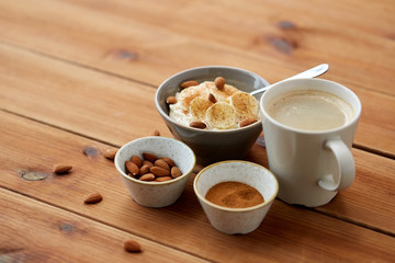 food and breakfast concept - oatmeal porridge in bowl with sliced banana, almond nuts and cinnamon and cup of coffee on wooden table
