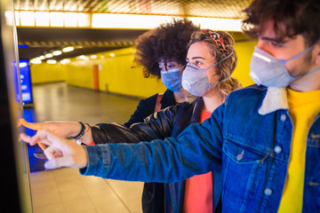 Fototapeta premium Three multiethnic friends wearing medical mask protecting from pollution and virus using touchscreen