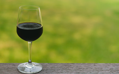 A glass of red wine on wooden table with blurry green background.