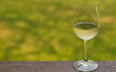 A glass of white wine on wooden table with blurry green background.