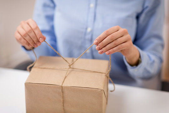 delivery, mail service, people and shipment concept - close up of woman packing parcel or gift box and tying rope