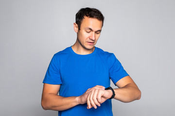 Portrait of a smiling young sportsman adjusting his wristwatch and looking at camera isolated over gray background