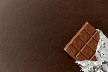 sweets, confectionery and food concept - milk chocolate bar in foil wrapper on brown background