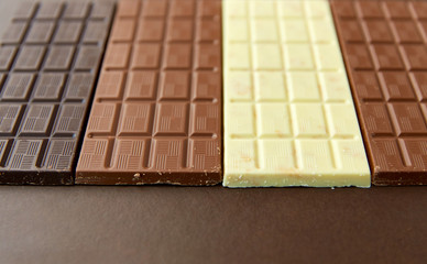 sweets, confectionery and food concept - milk, dark and white chocolate bars on brown background