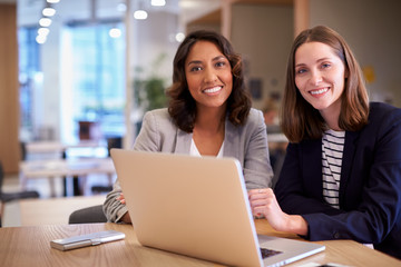 Portrait Of Two Businesswomen With Laptop Collaborating On Project In Office Together