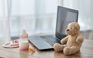 feeding and technology concept - bottle with baby milk formula, laptop computer, teddy bear toy and...