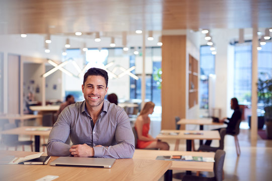 Portrait Of Businessman At Desk In Modern Office Work Space With Closed Laptop