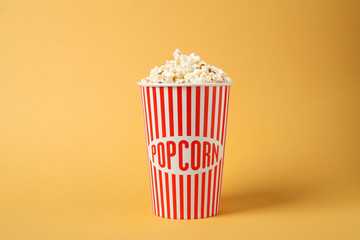 Delicious popcorn in paper cup on yellow background