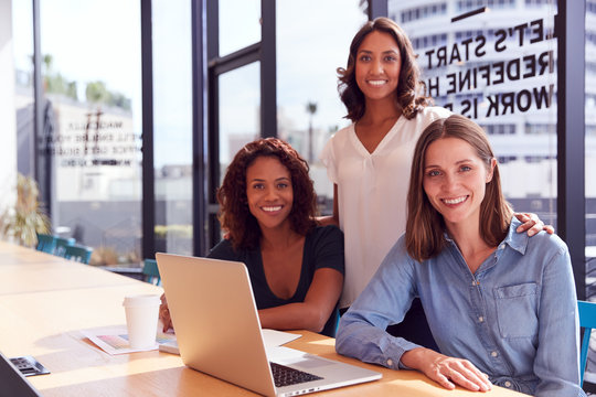 Portrait Of Three Businesswomen With Laptop At Desk By Window In Office Collaborating On Project