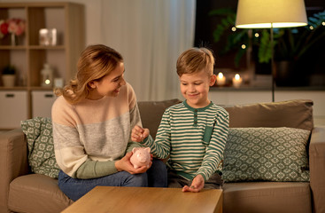 money, family and people concept - happy smiling mother and thrifty little son putting euro coin to piggy bank at home