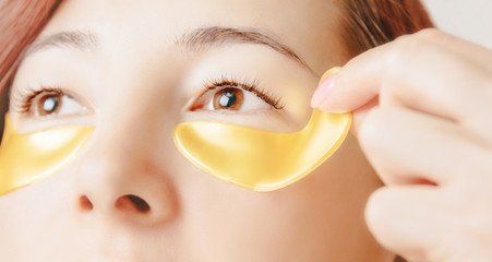 Woman applying golden collagen mask patch under eye.