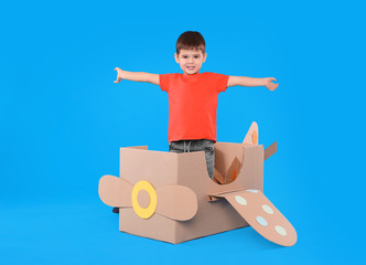 Cute little child playing with cardboard airplane on light blue background