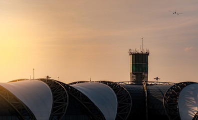 Airport roof and air traffic control tower in the airport with international flight plane flying on the sky. Airport traffic control tower for control airspace by radar. Aviation technology.