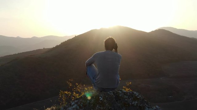 Concept of achievement and illumination at the end of the path as a reward for the fight A man sitting on top of a cliff watches the sunset in the mountains