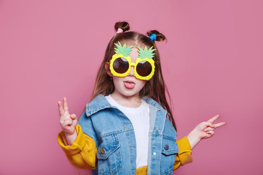 Summer fashion concept. cheerful little girl in big pineapple sunglasses on pink background