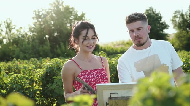 Portrait of happy artists' couple rejoices during painting in green bushes field